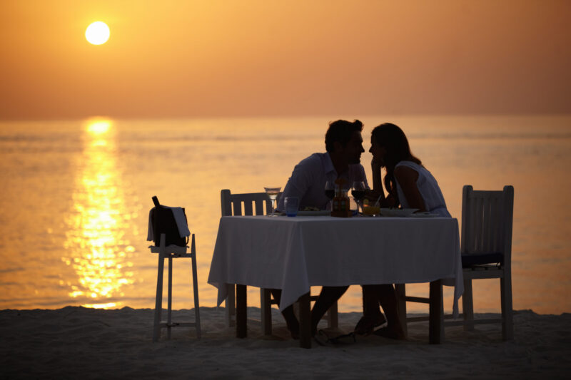 ocean sunset and couple at table for romantic valentines day date at the beach in Bali in silhouette