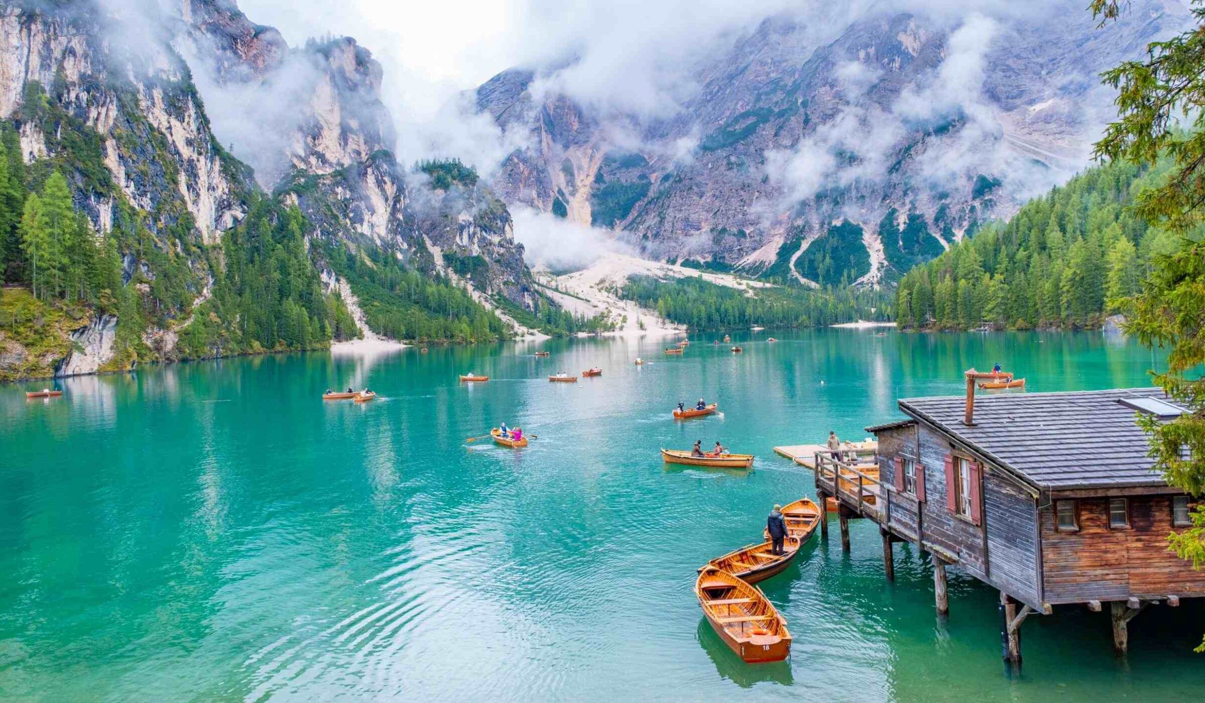 Small boats floating on a turquoise lake surrounded by mountains in the Dolomites