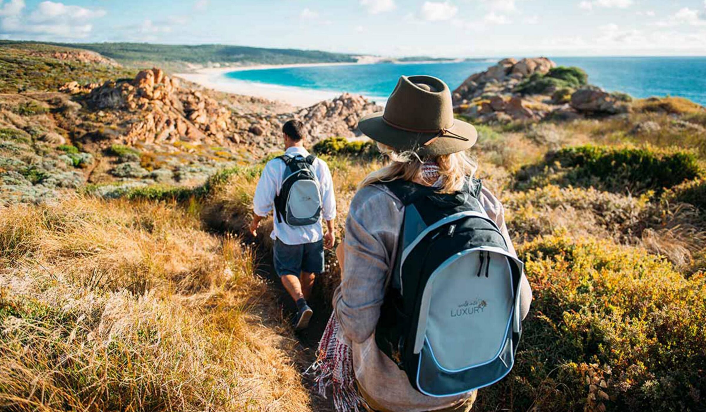 Two people hiking a coastal trail in Australia. One wears a backpack reading walk into LUXURY.