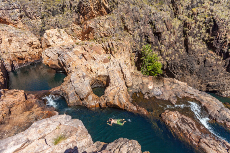 A person swimming in a natural rock pool surrounded by rocky cliffs in Australia.