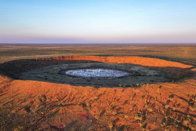 Aerial view of a massive circular meteorite crater with a white center in the arid landscape of Australia.