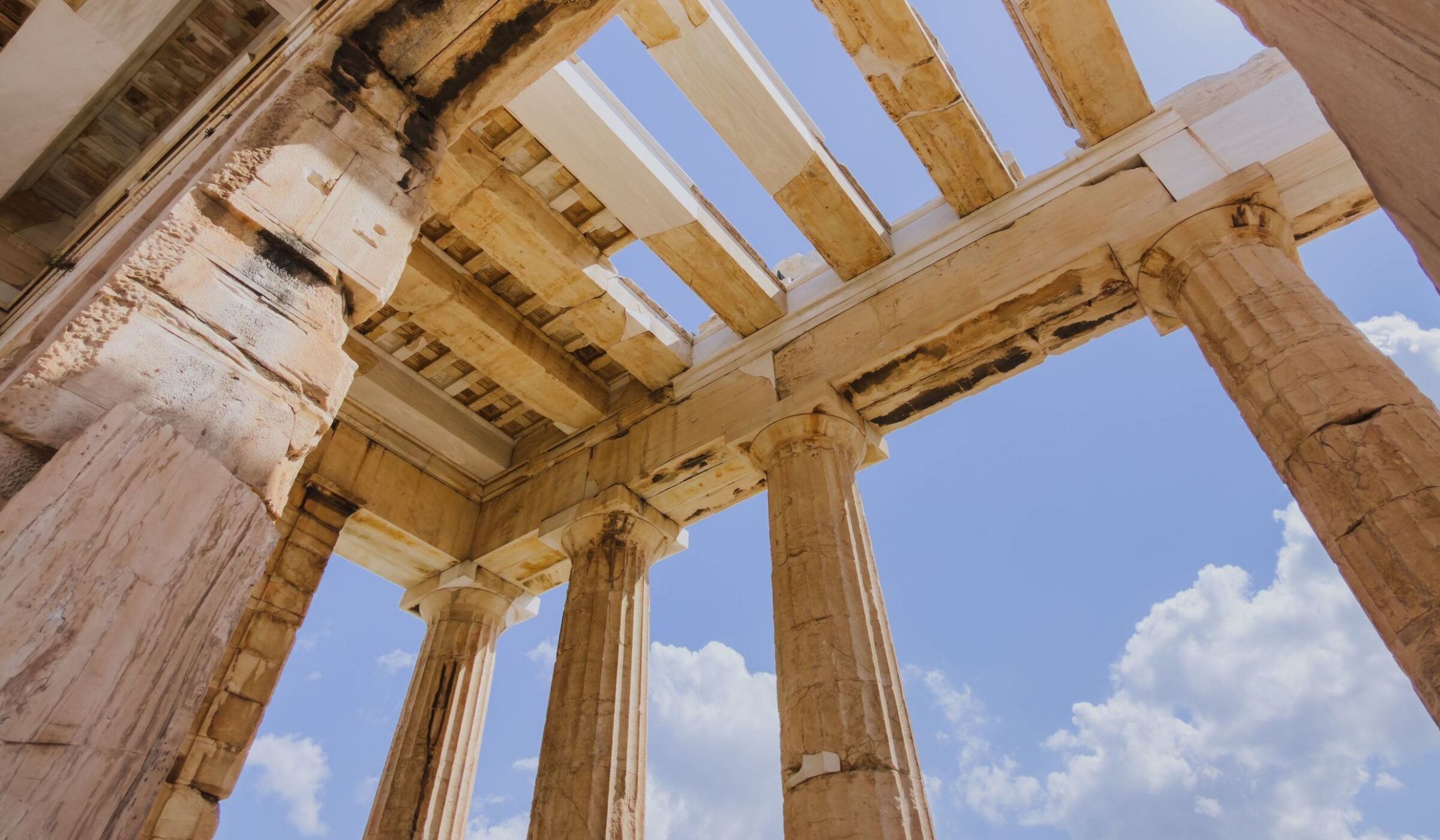 Low angle view looking up at the ancient stone Doric columns and roof beams of the Parthenon in Athens, Greece.