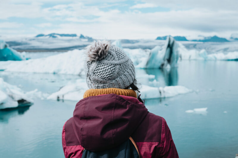 Person in a knit hat looking at large blue icebergs floating in a glacial lagoon on a polar safari.