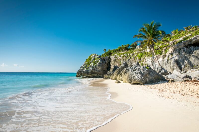 Turquoise waves crash against the white sand beach at the Tulum ruins in Mexico.