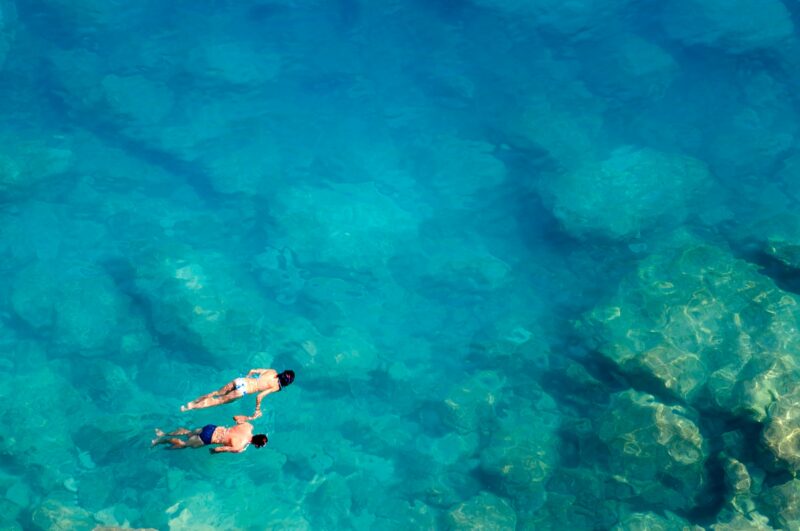 Aerial view of two people snorkeling in clear turquoise water on luxury Honeymoons.