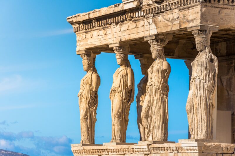 Karyatides statues, Erehtheio, on the Acropolis in Athens, Greece, with a blue sky behind.