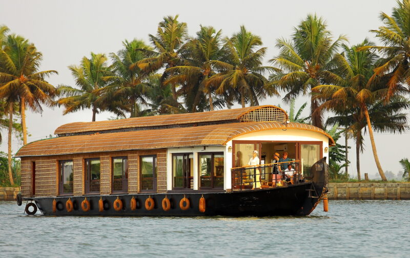 A houseboat on a Spice Routes Cruise sailing along the Keralan Backwaters in India, surrounded by palm trees.