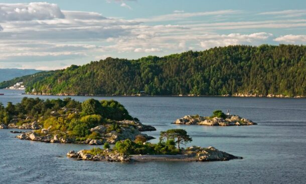 Small green islands in a calm sea with a large forested hill in the background under a bright sky.