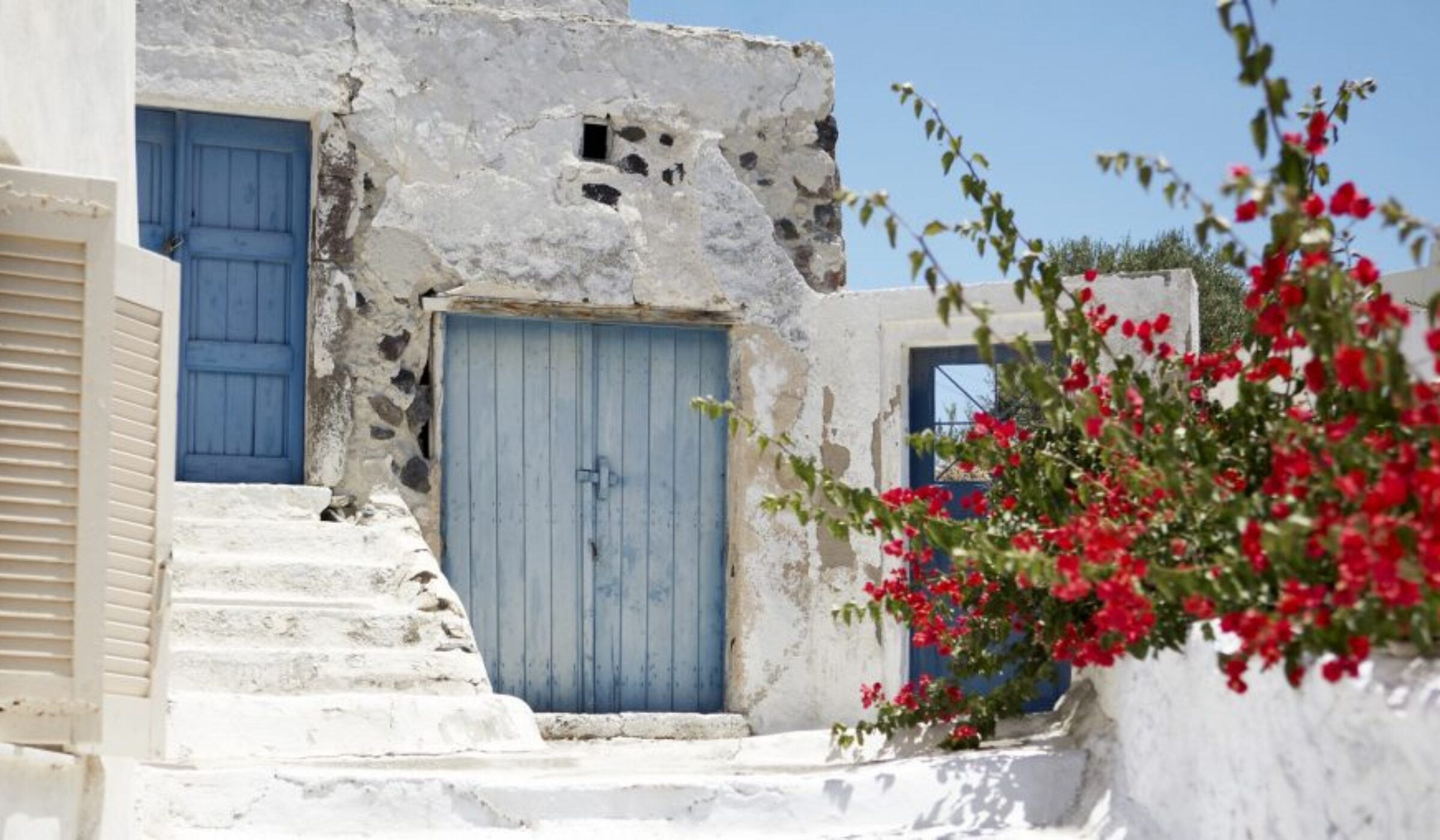 Luxury Greece Tours - Red bouganvellia set against whitewashed stone building with blue wooden doors